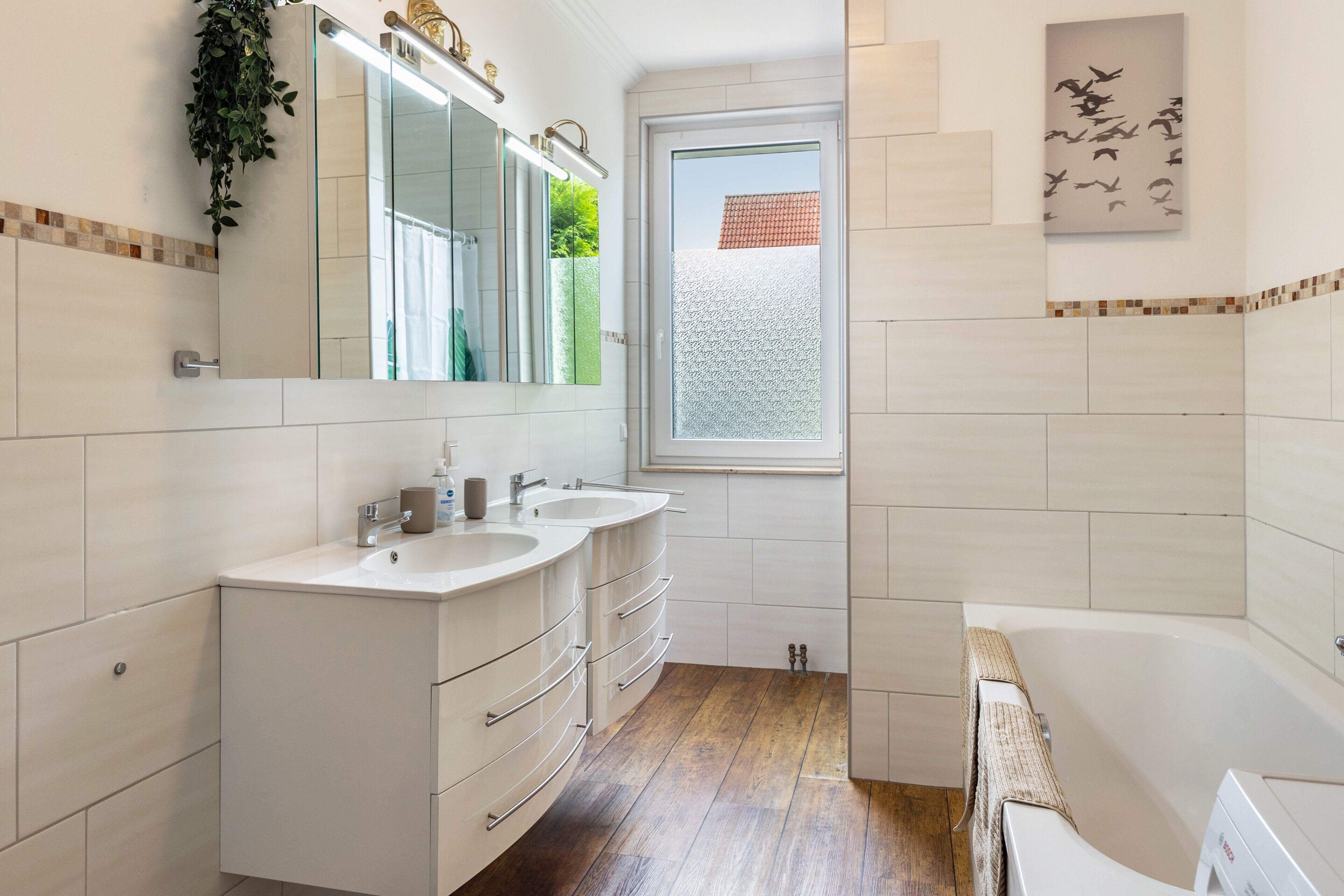 A bathroom with two sinks, a mirror, a window, and a bathtub.