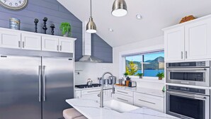 A modern kitchen with stainless steel appliances, white cabinetry, and a large window offering a scenic view.