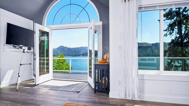 A room with a large arched window, a telescope on a tripod, and a view of a lake and mountains.