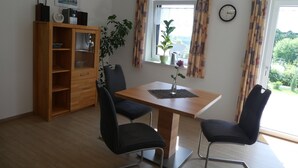 A dining area with a wooden table, four black chairs, a wooden cabinet, a potted plant, and a window with curtains.