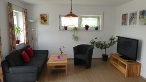 A living room with a sofa, armchair, TV stand, and potted plants.