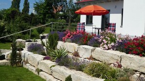 A white building with a red roof, a red umbrella, and a stone wall with colorful flowers.