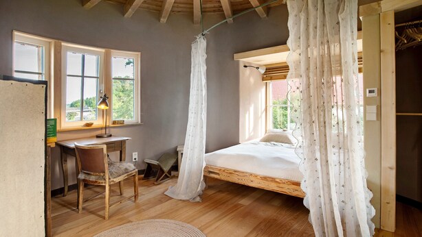 Ein Schlafzimmer mit einem Holzbett, einem Schreibtisch, einem Stuhl und einem Fenster mit Vorhängen.