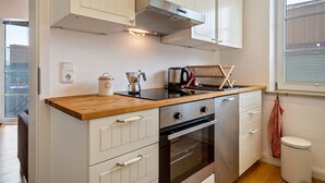 Een keuken met witte kasten, een houten aanrecht, een fornuis en een raam.