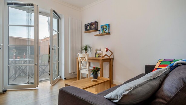 Een woonkamer met een bank, een houten salontafel, een stoel, een kleine tafel met een plant en een boekenkast met boeken en een wereldbol.