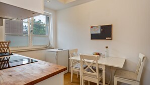 Een keuken met een houten aanrecht, witte stoelen, een kleine tafel en een raam met jaloezieën.