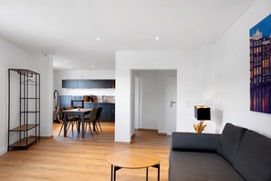 Una sala de estar moderna con un sofá, una mesa de comedor y sillas. En el fondo, se ve una cocina con armarios y un fregadero.
