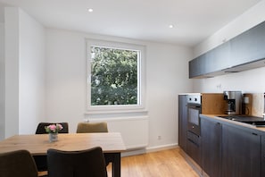 Een moderne keuken met een groot raam, ingebouwde apparatuur en een eethoek met een tafel en stoelen.