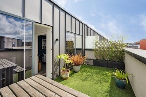 A modern building with a glass door entrance, a small outdoor seating area with a wooden bench, and potted plants on a grassy rooftop.