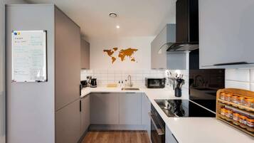Une cuisine moderne avec un réfrigérateur blanc, un four à micro-ondes, une machine à café et un évier. Un grand planisphère est accroché au mur, et on y trouve également un petit îlot central doté d’un évier et d’un plan de travail.