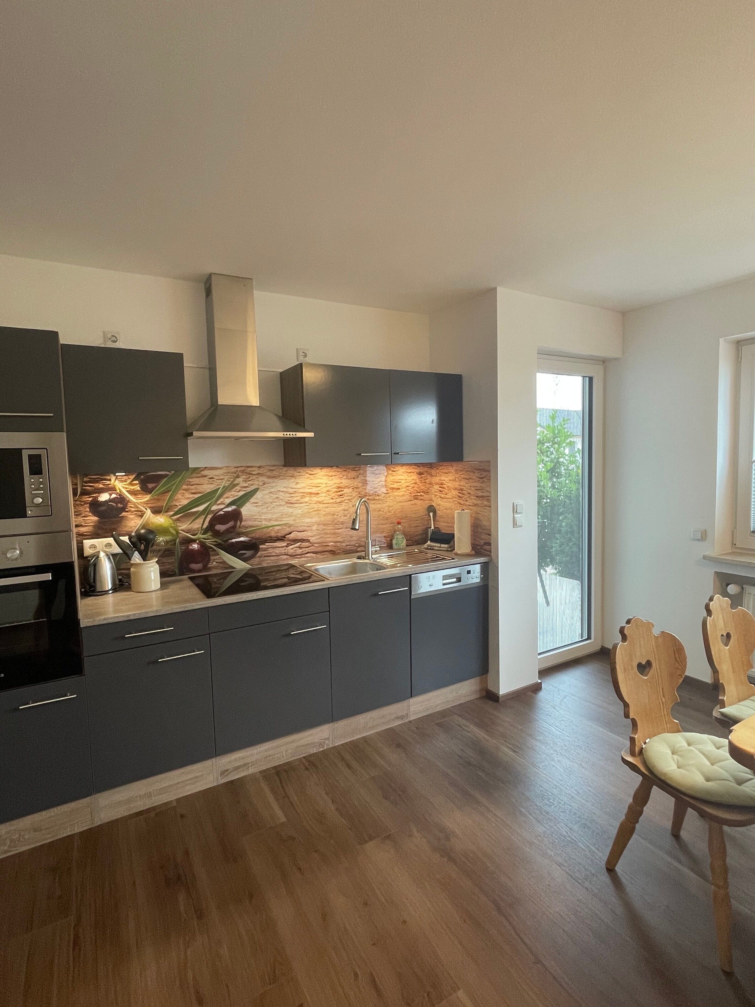A modern kitchen with dark cabinetry, a built-in oven, and a large window.