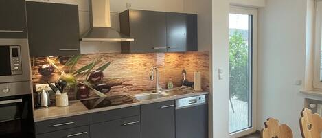 A modern kitchen with dark cabinetry, a built-in oven, and a large window.