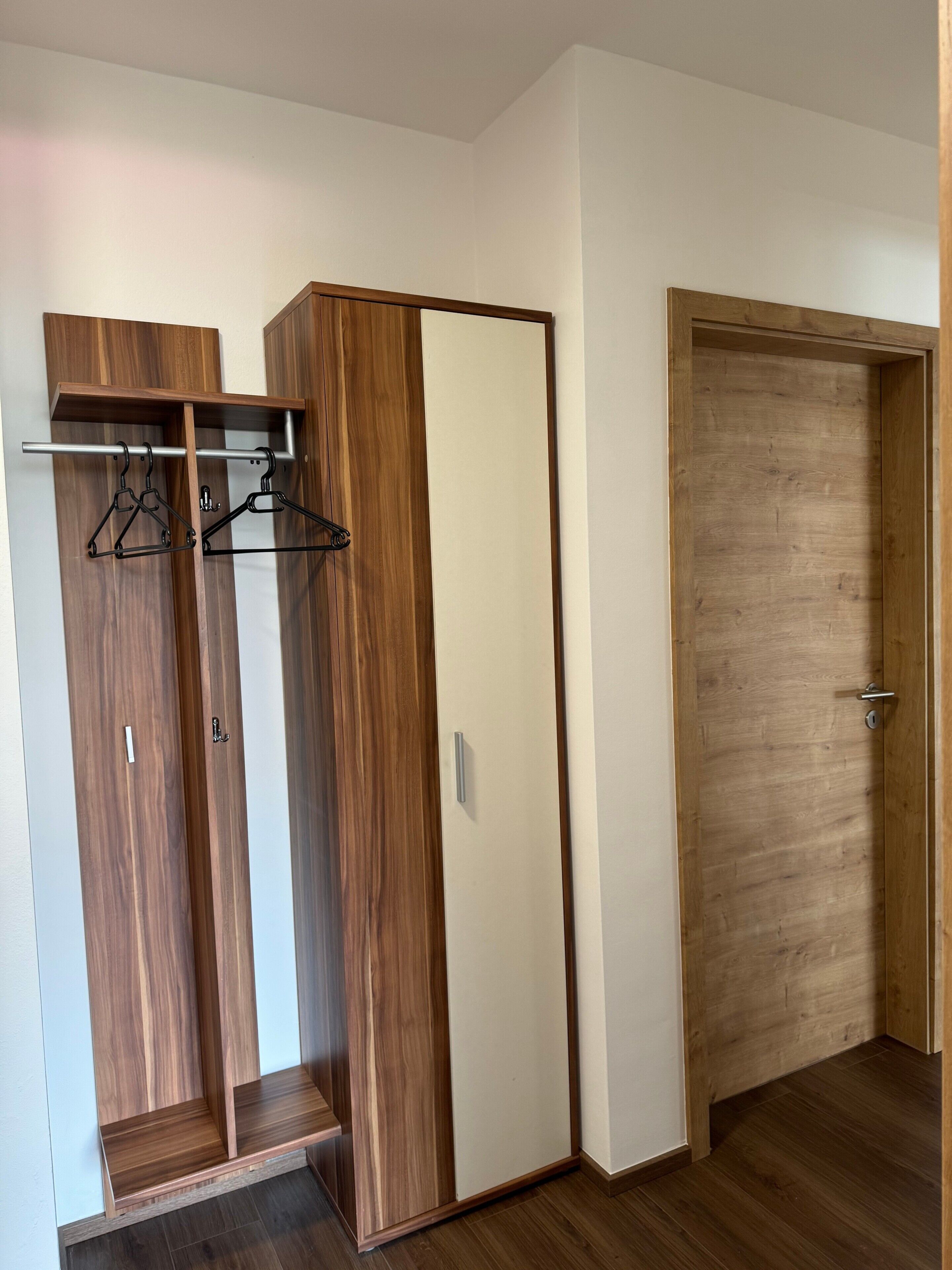 Una habitación con un armario de madera, un perchero y una puerta de madera.