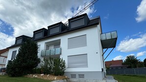 Un moderno edificio de dos pisos con un balcón, un pequeño jardín y un camino de entrada de grava.
