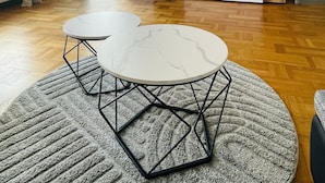 Una sala de estar moderna con una televisión de pantalla plana, dos mesas redondas, un aparador de madera y vistas al exterior.
