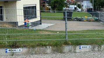 Ein eingezäunter Parkbereich mit Kiesbefestigung, ein Gebäude mit weißer Fassade und ein sichtbarer Hydrant.