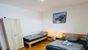 Un dormitorio con dos camas, un armario, un cuadro en la pared y un suelo de madera con diseño espiga.