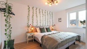 Une chambre à coucher avec un lit, des tables de chevet, une fenêtre et du lierre décoratif.