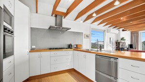 A modern kitchen with white cabinetry, a stainless steel dishwasher, and a wooden countertop. - Beach House (Separation Creek)