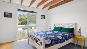 A bedroom with a bed, a nightstand, a lamp, and a view through a sliding door. - Beach House (Separation Creek)