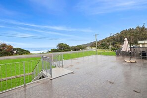 A covered outdoor area with a metal railing, a concrete floor, and a view of a road and greenery. - Beach House (Separation Creek)