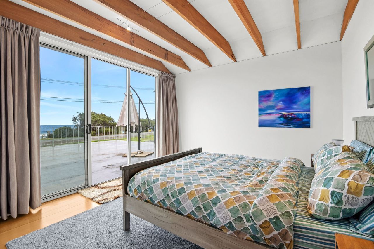 Ein Schlafzimmer mit einem Bett, einem Gemälde und Blick durch eine Glastür.