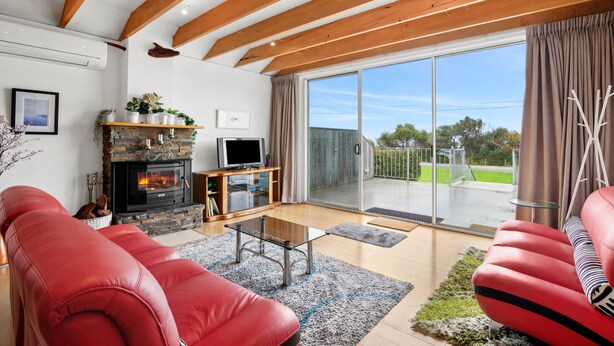 A living room with a fireplace, a television, and a large sliding glass door leading to an outdoor area. - Beach House (Separation Creek)