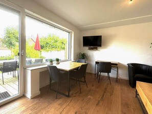 Una habitación con una mesa de comedor, sillas, un televisor montado en la pared y un ventanal corredero que da a un espacio exterior.