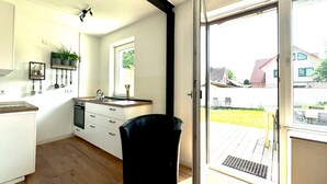 A modern kitchen with white cabinets, a black chair, and a sliding glass door leading to a deck. - Holiday Home 'Ferienhaus Ahaus' with Private Terrace, Private Garden and Wi-Fi (Ahaus)
