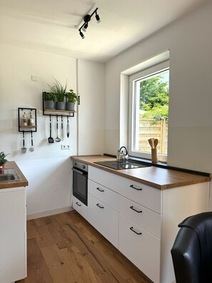 Una cocina moderna con armarios blancos, encimera de madera, un hervidor y una ventana con vistas al verdor.
