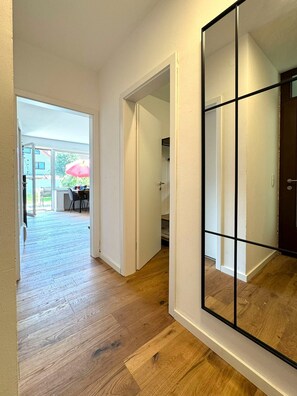 Un couloir doté d’un plancher en bois, de murs blancs et d’un grand miroir.