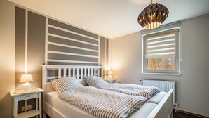 A bedroom with a bed, bedside tables, a lamp, a radiator, and a window with blinds. - Apartment 'Strandläufer' with Shared Garden and Wi-Fi (Westerholz)