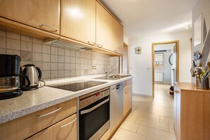 Una cocina moderna con armarios de madera, horno empotrado, lavavajillas y una encimera con cafetera.