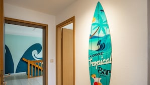 A surfboard-shaped sign with 'Summer Tropical Bar' text, a wooden staircase, and a door leading to a room with a blue wall and a wave pattern. - Apartment 'Strandläufer' with Shared Garden and Wi-Fi (Westerholz)