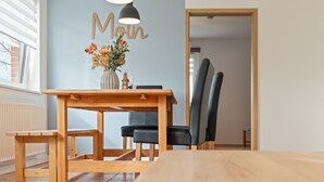 Un coin repas avec une table en bois, des chaises noires, un vase rempli de fleurs et un mur sur lequel est inscrit le mot « Moulin ».