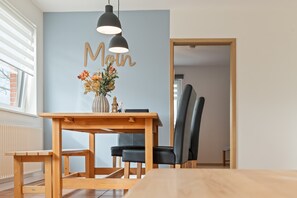 A dining area with a wooden table, black chairs, a vase with flowers, and a wall with the word 'Moulin' on it. - Holiday Apartment 'Ankerplatz' with Private Terrace, Shared Garden & Wi-Fi (Westerholz)