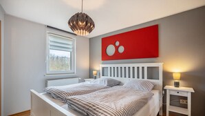 Une chambre à coucher avec un lit, des tables de chevet, une fenêtre et une œuvre d’art rouge accrochée au mur.