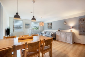 A modern kitchen with a dining table, chairs, pendant lights, a sofa, and a cabinet.