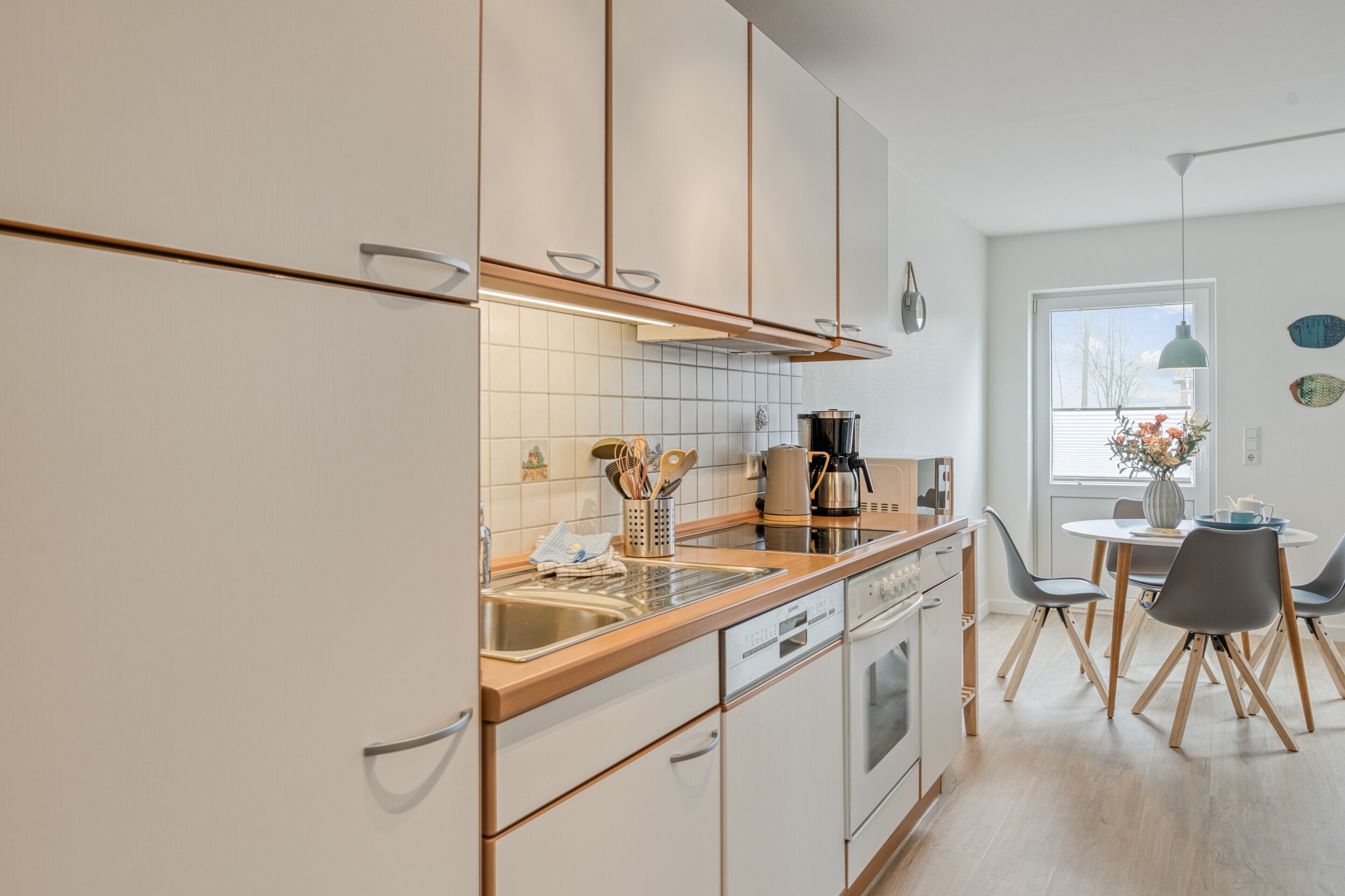 Een moderne keuken met witte kasten, een roestvrijstalen spoelbak, een koffiezetapparaat en een eethoek met een tafel en stoelen.
