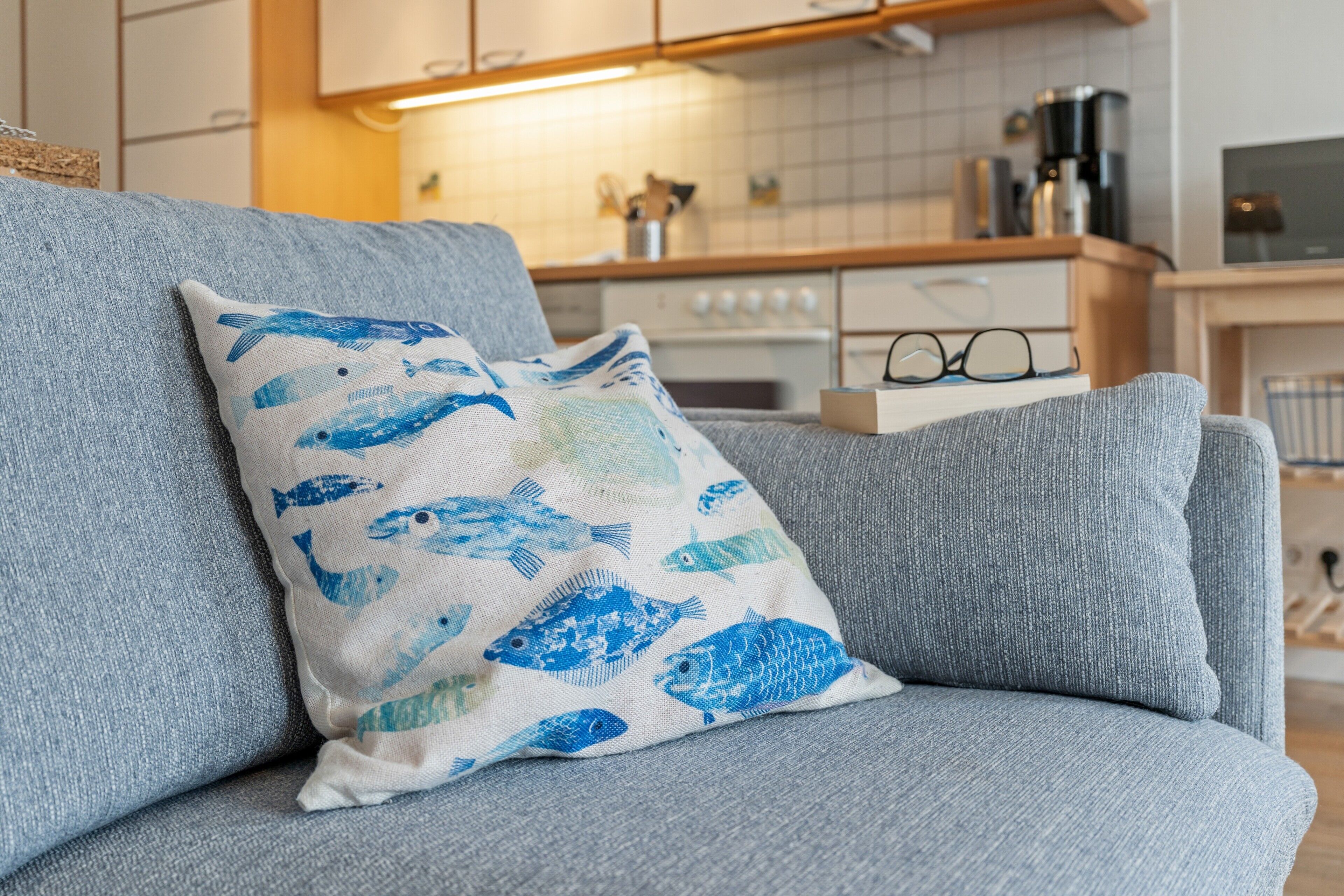Ein graues Sofa mit einem blau gestreiften Kissen und einer Brille auf einem Tisch.
