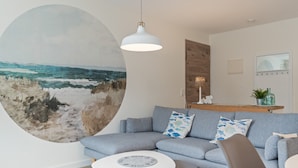 A modern living room with a grey sofa, a round coffee table, and a large abstract painting. - Apartment 'Küstenkind' with Private Terrace, Private Garden and Wi-Fi (Westerholz)