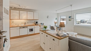 A modern kitchen with white cabinets, a wooden countertop, and a dining area with a table and chairs. - Apartment 'Küstenkind' with Private Terrace, Private Garden and Wi-Fi (Westerholz)