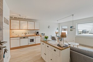 A modern kitchen with white cabinets, a wooden countertop, and a dining area with a table and chairs. - Apartment 'Küstenkind' with Private Terrace, Private Garden and Wi-Fi (Westerholz)