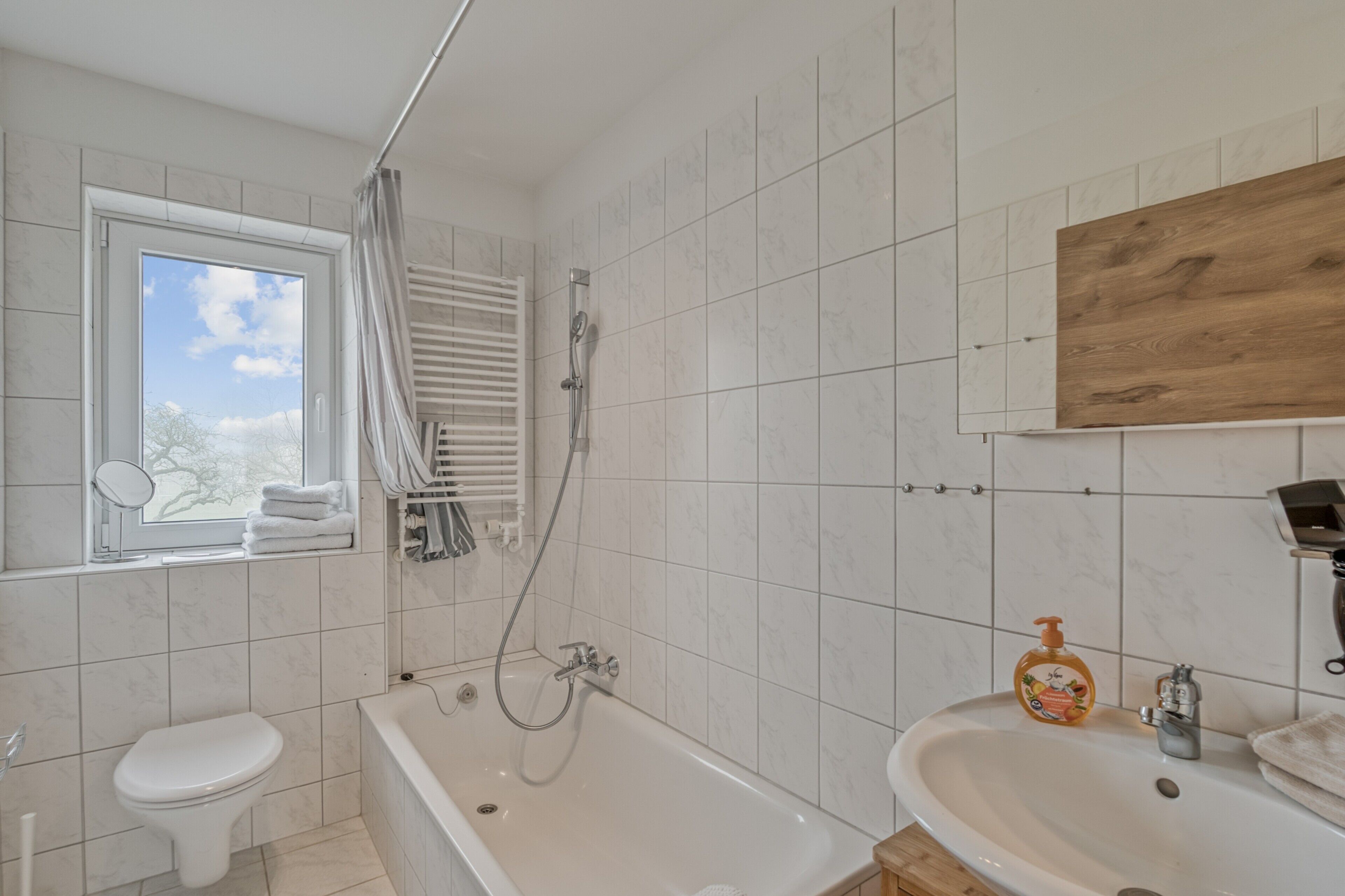 Ein Badezimmer mit Toilette, Badewanne und Waschbecken, einem Fenster mit Aussicht und einem Holzboden.