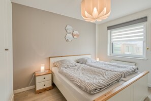 Quarto com cama, mesas de cabeceira, luminária pendente e janela com persianas.
