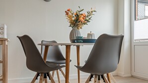 A dining area with a table, chairs, a vase with flowers, and a clock on the wall. - Apartment 'Küstenkind' with Private Terrace, Private Garden and Wi-Fi (Westerholz)
