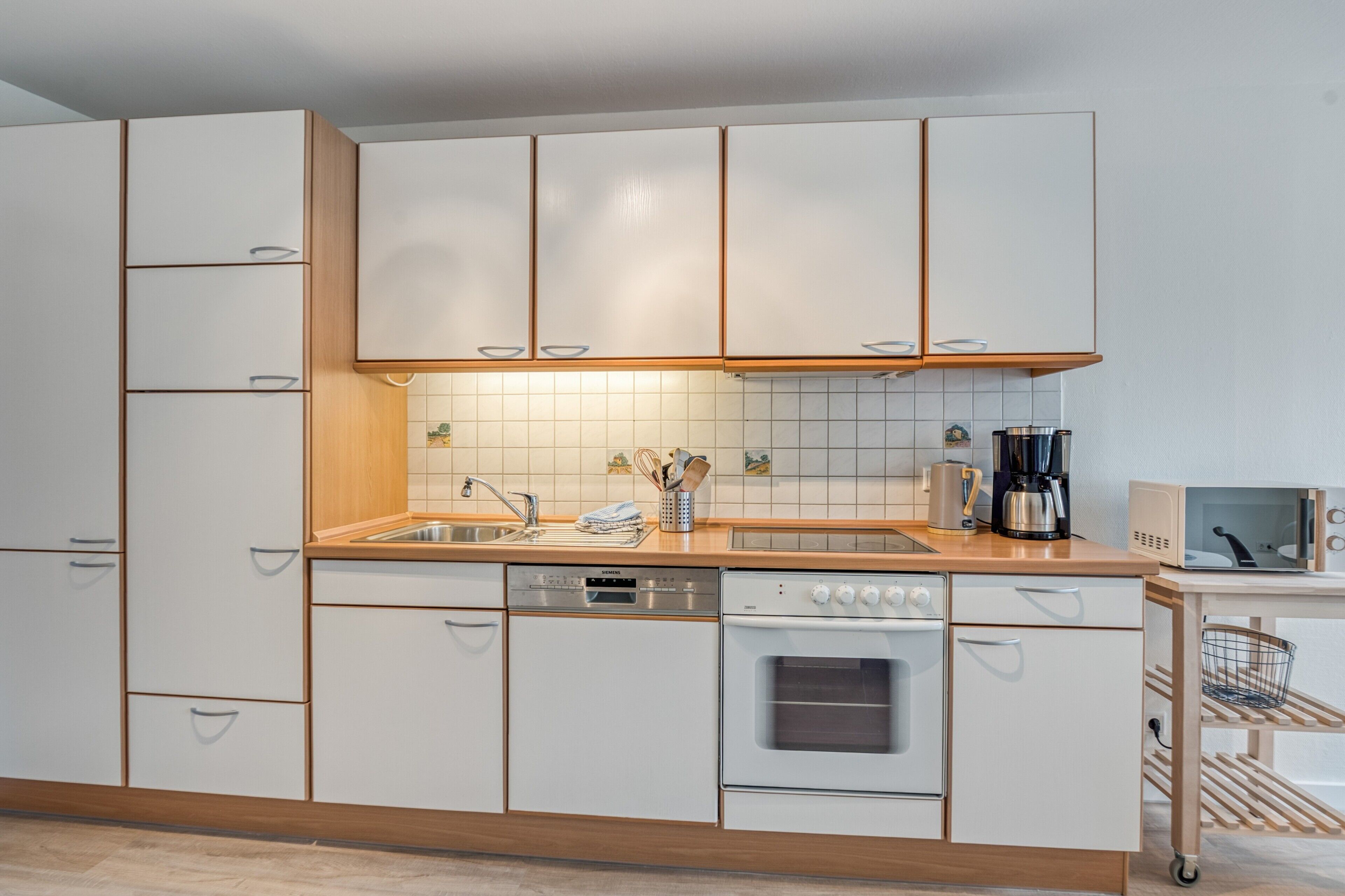 Una cocina moderna con armarios blancos, horno empotrado, cafetera y microondas.