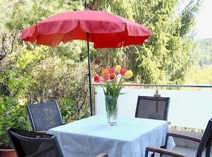 A table with a white tablecloth, a red umbrella, and a vase with flowers.