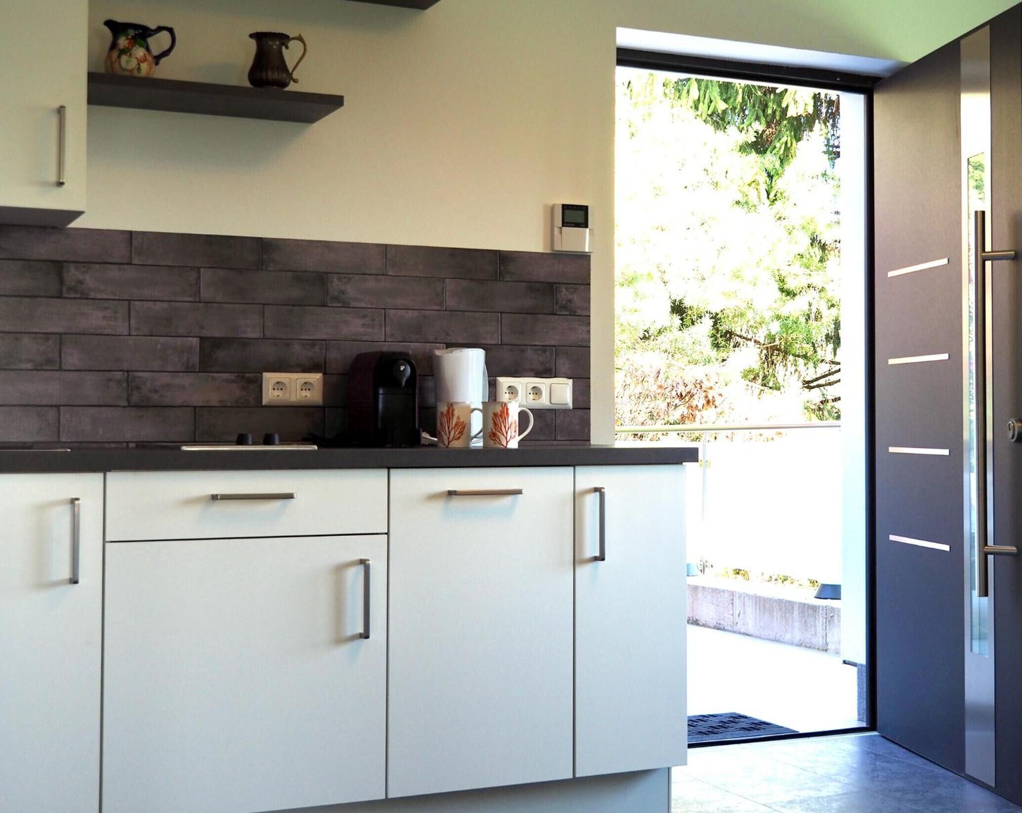 Een moderne keuken met witte kasten, een donkere spatwand en een koffiezetapparaat op het aanrecht.