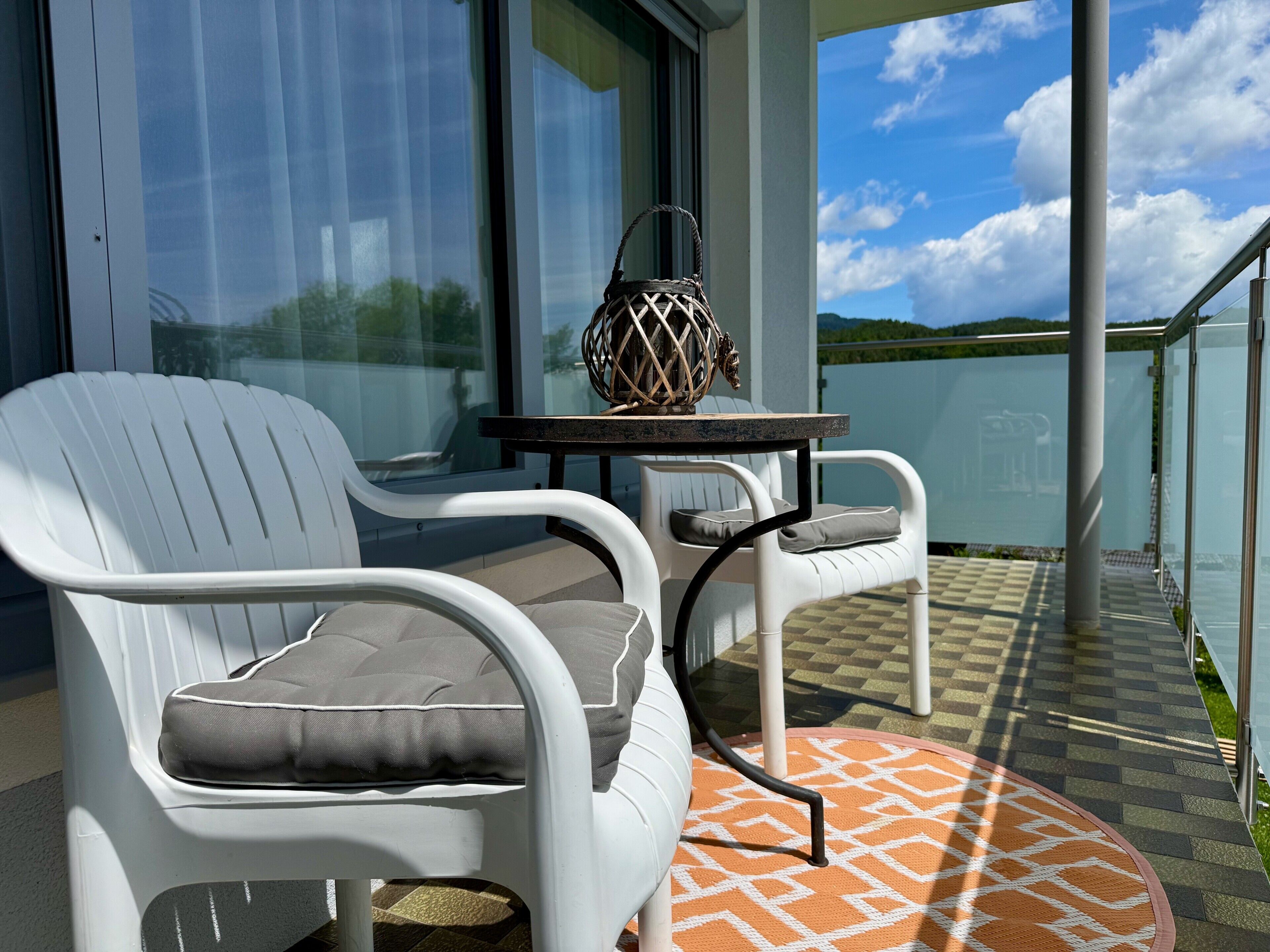 Un balcon avec des chaises blanches, une petite table et un objet décoratif.